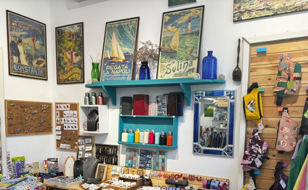Interior de atelier-boutique cu afișe vechi de turism înrămate, rafturi turcoaz cu sticle albastre și standuri cu bijuterii și obiecte făcute de mână