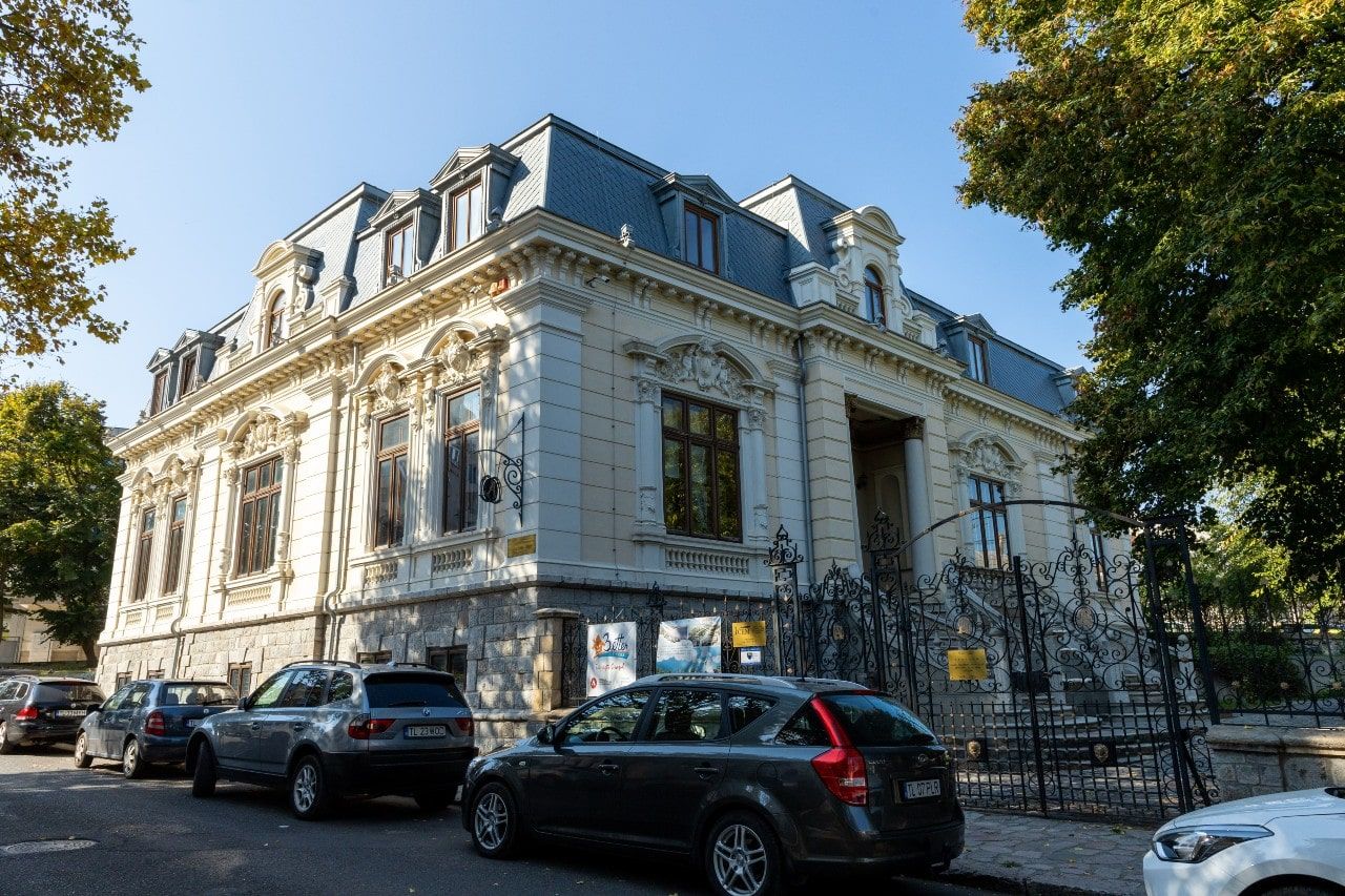 Fațada de secol XIX a Casei Avramide din Tulcea, cu ancadramente sculptate, acoperiș de tablă în pantă și gard din fier forjat, văzută de peste stradă