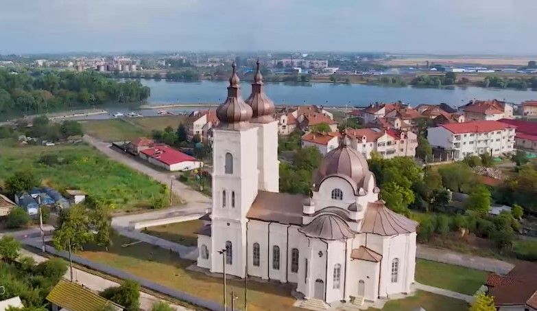 Vedere aeriană asupra bisericii albe cu două turle și cupole din Chilia Veche, cu satul în jur și brațul Chilia în fundal