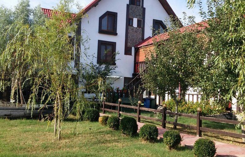Clădire de pensiune cu acoperiș roșu și mansardă, cu sălcii și gard de lemn în față, într-o curte cu gazon la Crișan